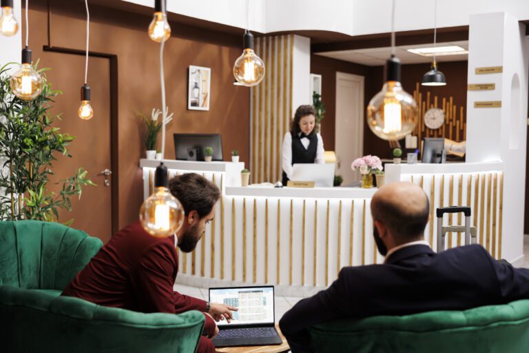 Two professionals review notes on laptop, creating buisness meeting in lounge area at luxury hotel. International representatives attend important conference to share experiences.